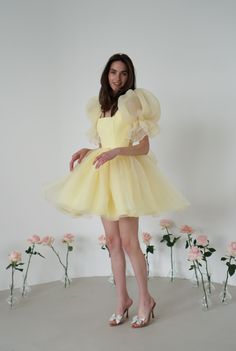 Introducing the Britney Dress in a delightful light yellow: a stunning creation crafted from delicate bubble organza. This lightweight dress features an elegant silhouette with a voluminous floating skirt that moves gracefully with every step. The charming puff sleeves add a whimsical touch, making it perfect for any special occasion. The Britney Dress is enclosed with delicate bow ties down the back, adding a romantic and feminine detail that completes the look. In light yellow, this dress exud Organza Puff Sleeve Wedding Dress, Wedding Puff Sleeve Dress With Ruffles And Balloon Sleeves, Spring Party Puff Sleeve Organza Dress, Spring Party Organza Puff Sleeve Dress, Yellow Organza Wedding Dress, Voluminous Balloon Sleeve Wedding Dress, Elegant Yellow Puff Sleeve Dress, Feminine Yellow Evening Dress, Spring Wedding Dress With Puff Balloon Sleeves