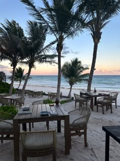 tables and chairs on the beach with palm trees in the foreground, at sunset