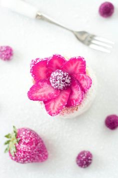 a strawberry cupcake topped with powdered sugar and a pink flower next to strawberries