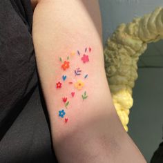 a woman's arm with colorful flowers on it and small hearts in the middle