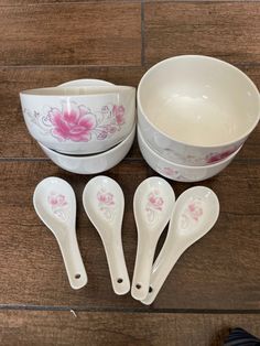 four white bowls with pink flowers and spoons next to each other on a wooden floor