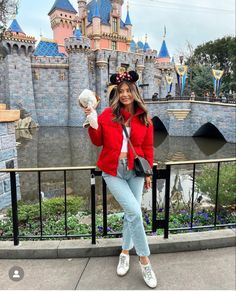 a woman poses for a photo in front of the castle at disneyland world, with her hand up