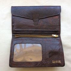 Vintage brown  leather bi-fold wallet, 1970s W 4 inches  10 cm H 6.5 inches  16.5 cm Inside left, tab and strap that give access to complete width and length of wallet back compartment. Three slip in pockets. Central metal zip gives access to another complete width and length of wallet back compartment. Right side has one slip in pocket for notes,  plus card pocket and stamps pocket, plus one vinyl window pocket.Rich dark brown textured leather with foil markings, made in China, real leather. Ve Vintage Leather Trifold Wallet With Coin Pocket, Vintage Brown Bifold Wallets With Card Slots, Vintage Brown Bifold Wallet With Card Slots, Vintage Brown Bifold Wallet With Interior Card Slots, Retro Bifold Wallets With Coin Pocket, Vintage Trifold Wallet With Coin Pocket For Travel, Retro Bifold Wallet For Everyday Use, Retro Leather Wallet With Coin Pocket, Vintage Leather Bifold Wallet