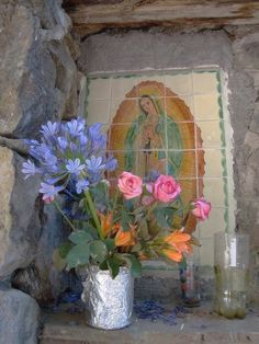 colorful flowers in a silver vase sitting on a stone ledge next to a tile wall