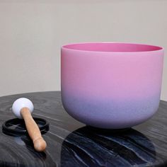 a pink and blue bowl sitting on top of a table next to a wooden mallet