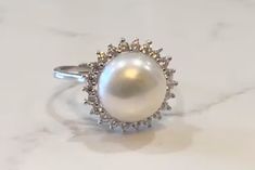 The Pearl is the only gem created in living being. When something penetrates an oyster's shell, it doesn't reject it; it embraces it, encases it & turns it into something beautiful. ♥️ This stunning ring features a freshwater pearl encircled by lustrous crystals. Available in silver or gold. Adjustable, size 5-8 PRODUCT DETAILS: 10mm AAA freshwater button iridescent pearl Luster - High Setting: sterling silver or 14kt gold plated with crystal mount Size: Adjustable, Size 5-8 Materials: Freshwate Timeless Diamond White Pearl Ring, Diamond White Pearl Ring With Gemstone For Anniversary, Pearl Jewelry With Prong Setting, Timeless Round Pearl Ring, Anniversary Pearl Ring With Round Cut Gemstone, Pearl Charm Promise Ring, Elegant White Halo Ring With Gemstone, Diamond White Akoya Pearl Ring, Diamond Pearl Ring With Pearl Drop