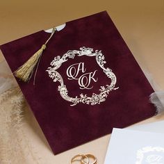 two wedding rings are sitting on top of a burgundy paper with a gold monogrammed ring