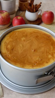 a cake in a pan on a table with apples and cinnamon sticks around the edges