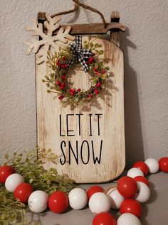 a wooden sign that says let it snow with red and white balls on the ground