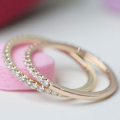 two gold wedding rings sitting on top of a pink ring box next to each other