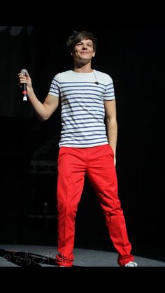 a man standing on top of a stage with a microphone in his hand and wearing red pants