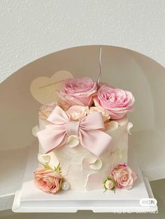 a white cake with pink flowers and a bow on top is sitting on a shelf