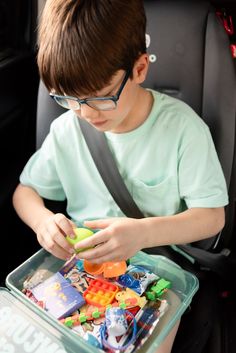 a young boy sitting in the back seat of a car playing with toy cars and building blocks