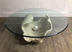 a glass table with a shell shaped base on the bottom and a ball in the middle