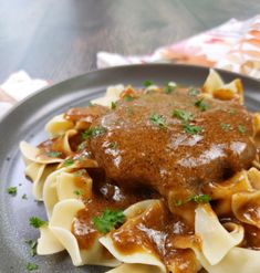 a black plate topped with pasta covered in gravy and meat sauce on top of it