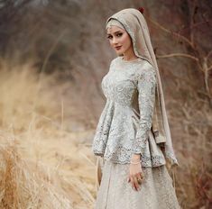 a woman wearing a white dress and head scarf standing in tall grass with her hands on her hips