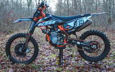 an orange and black dirt bike parked on top of leaves in front of some trees