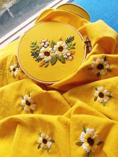 a yellow shirt with white daisies on it is sitting next to a small cross - stitch bag