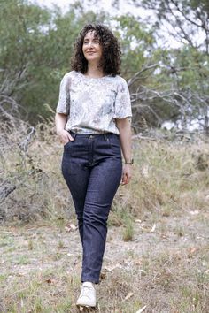 a woman is walking in the grass with her hand on her hip and smiling at the camera