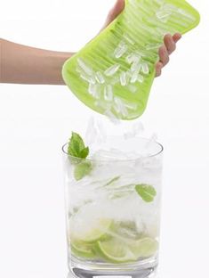 a person is holding a green strainer over ice cubes with mint leaves on top