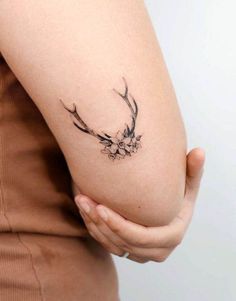 a woman's arm with a tattoo on it that has flowers and antelope