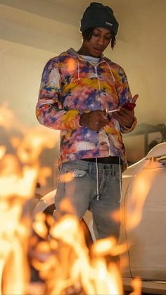 a young man standing in front of a fire with his hands on his hips while looking at the phone