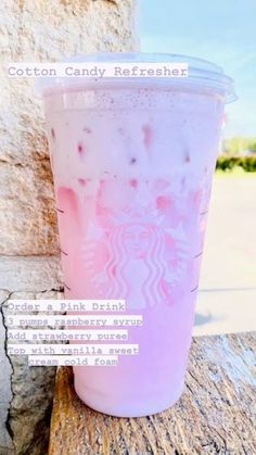 a pink drink sitting on top of a wooden table next to a stone wall with the caption cotton candy refresher