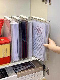 a person is pointing at files on a shelf