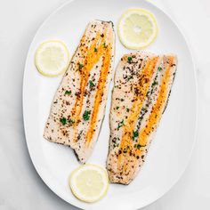 two fish fillets on a white plate with lemon slices