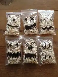 six bags of popcorn with the faces of cats and bats drawn on them, sitting on a wooden table