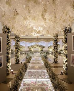 an elaborately decorated hall with white flowers and greenery on the ceiling is lit by chandeliers