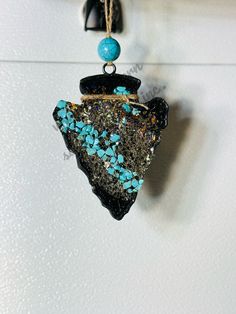 a piece of jewelry hanging from a hook on a white wall next to a blue bead necklace