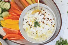 a bowl filled with white sauce surrounded by sliced carrots, cucumbers and celery