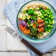 a bowl filled with vegetables and rice on top of a blue towel next to a fork