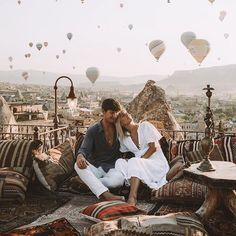 a man and woman sitting on top of a rug in front of hot air balloons