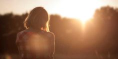 a woman standing in front of the sun with her back turned to the camera,