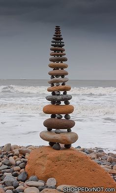 a stack of rocks sitting on top of a sandy beach next to the ocean under a cloudy sky