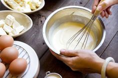 two hands whisk eggs into a bowl on a wooden table with other ingredients