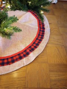 a christmas tree skirt is on the floor next to a small fir tree with red and black trim