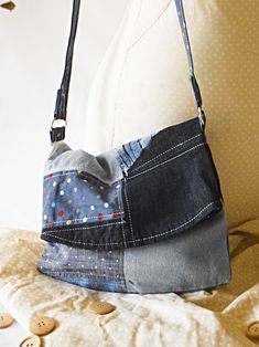 a purse made out of old jeans is sitting on a couch with buttons scattered about it