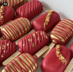 some red and gold decorated cookies in a white box with wooden spoons next to them