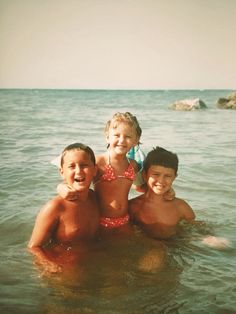 three children are in the water posing for a photo on a sunny day at the beach