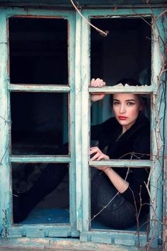 a woman sitting on the window sill with her hands behind her head and looking out