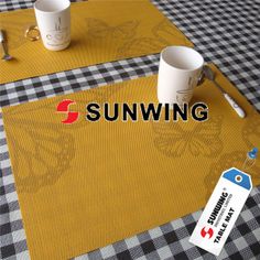 two coffee mugs sitting on top of a yellow place mat with the word sunwing printed on it