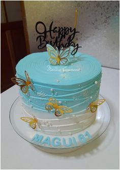 a blue cake with butterflies on it sitting on top of a white tablecloth covered table