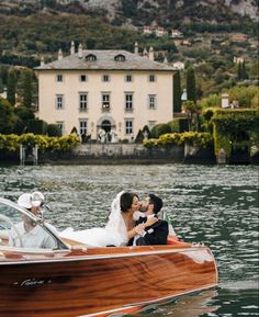 a bride and groom are kissing in a boat on the water near a large house