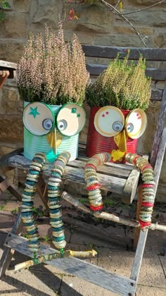 two owls made out of tin cans sitting on a bench with flowers in the back