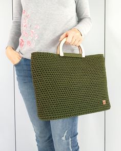 a woman holding a green purse with holes in the front and bottom, while standing against a white wall