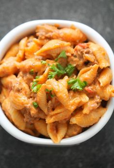 a white bowl filled with pasta covered in sauce and parsley on top of a table