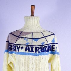 a white sweater with blue and grey designs on the front is hanging from a wooden hanger